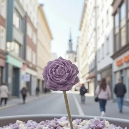 Petite pivoine vieux rose Lulu Baladine placée sur un bol fleuri au cœur d’une rue citadine animée.
