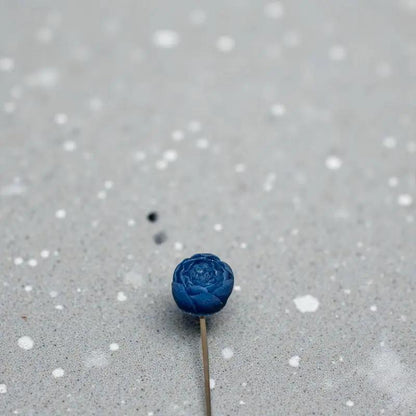 Petite renoncule bleu en cire artisanale, fleur poétique posée sur derrière béton  – Lulu Baladine