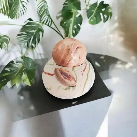Pierre massage posée sur son socle double. 
Le tout est posée sur une table avec en fond une herbe exotique 