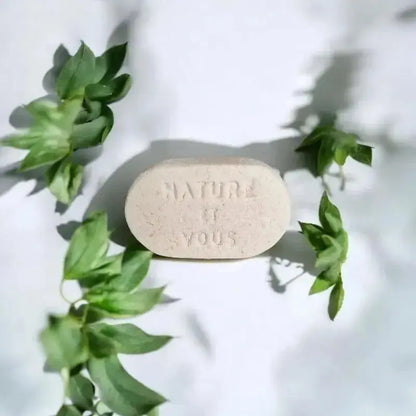 Porte-savon en argile naturelle beige gravé « Nature et Vous », accessoire écologique pour salle de bain zéro déchet, présenté sur fond blanc avec des feuilles vertes décoratives.