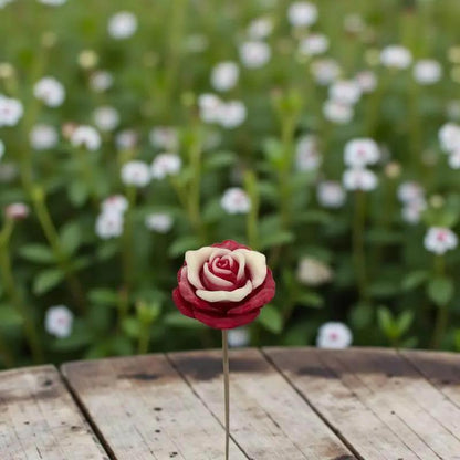 Rose moyenne bordée rouge en cire artisanale, fleur décorative poétique sur une table en bois dans un jardin fleuri – Lulu Baladine