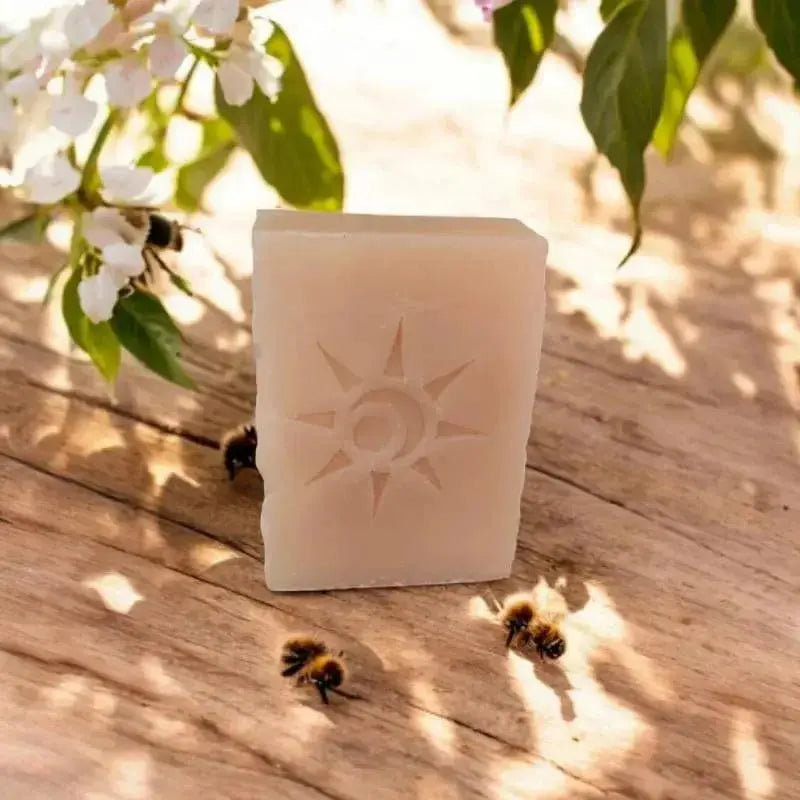 savon artisanal saponifié à froid gravé soleil posé sur planche bois avec abeilles et fleurs blanches