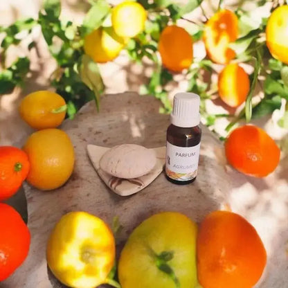 fiole ambrée d’extrait de parfum agrumes entourée d’oranges et de citrons, production artisanale près de Jonzac
